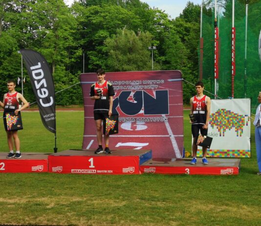 na zdjęciu znajduje je sie podium a na nim trzech mężczyzn w strojach sportowych, odbierają medale