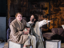 Scena ze spektaklu „Matka Courage i jej dzieci” w Teatrze Dramatycznym im. Aleksandra Węgierki w Białymstoku. Dwie aktorki w kostiumach siedzą na scenie, a jedna z nich wyciąga rękę w dramatycznym geście.