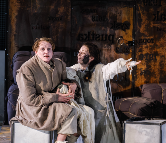 Scena ze spektaklu „Matka Courage i jej dzieci” w Teatrze Dramatycznym im. Aleksandra Węgierki w Białymstoku. Dwie aktorki w kostiumach siedzą na scenie, a jedna z nich wyciąga rękę w dramatycznym geście.
