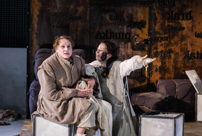 Scena ze spektaklu „Matka Courage i jej dzieci” w Teatrze Dramatycznym im. Aleksandra Węgierki w Białymstoku. Dwie aktorki w kostiumach siedzą na scenie, a jedna z nich wyciąga rękę w dramatycznym geście.